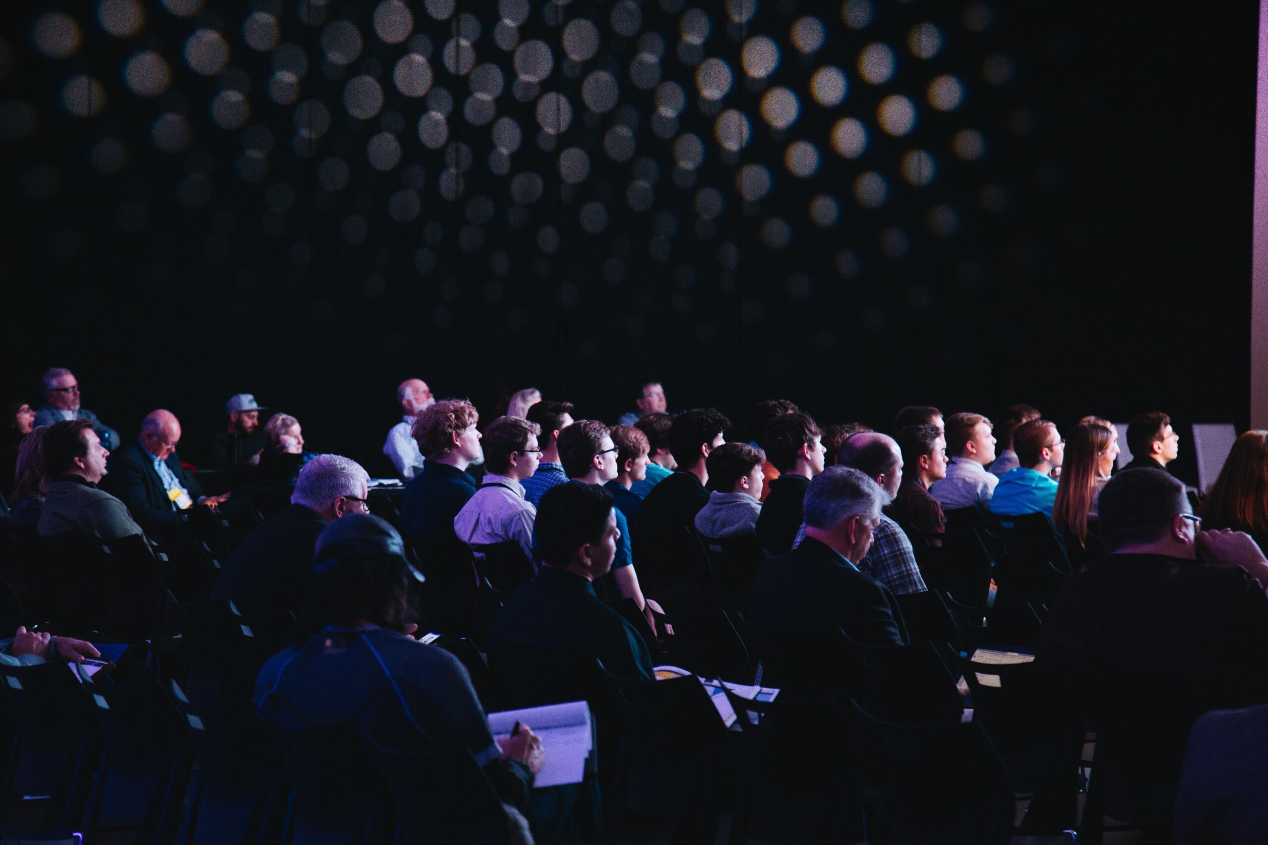 A conference hall full of guests sat on chairs watching a presentation