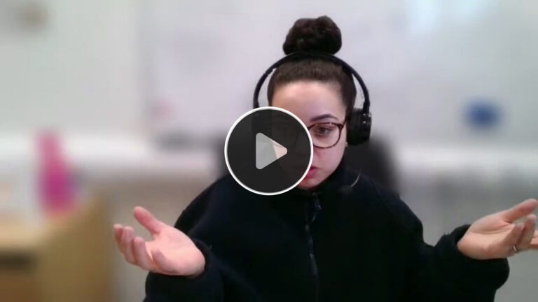 Mickella Nikoi wearing glasses and a headset, gesturing with both hands during a video call, explaining her thoughts on Prospectus Plus; the background is blurred, and the video play icon is overlaid in the centre.