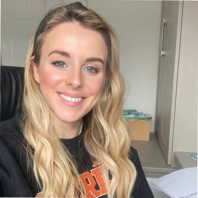 A photographic portrait of Bethan Evans, a white female, with long length blonde hair. She is wearing a graphic black tee.